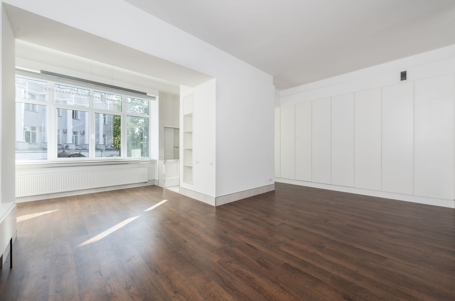 Helle, leer geräumte Wohnung mit dunklem Holzboden und großer Fensterfront